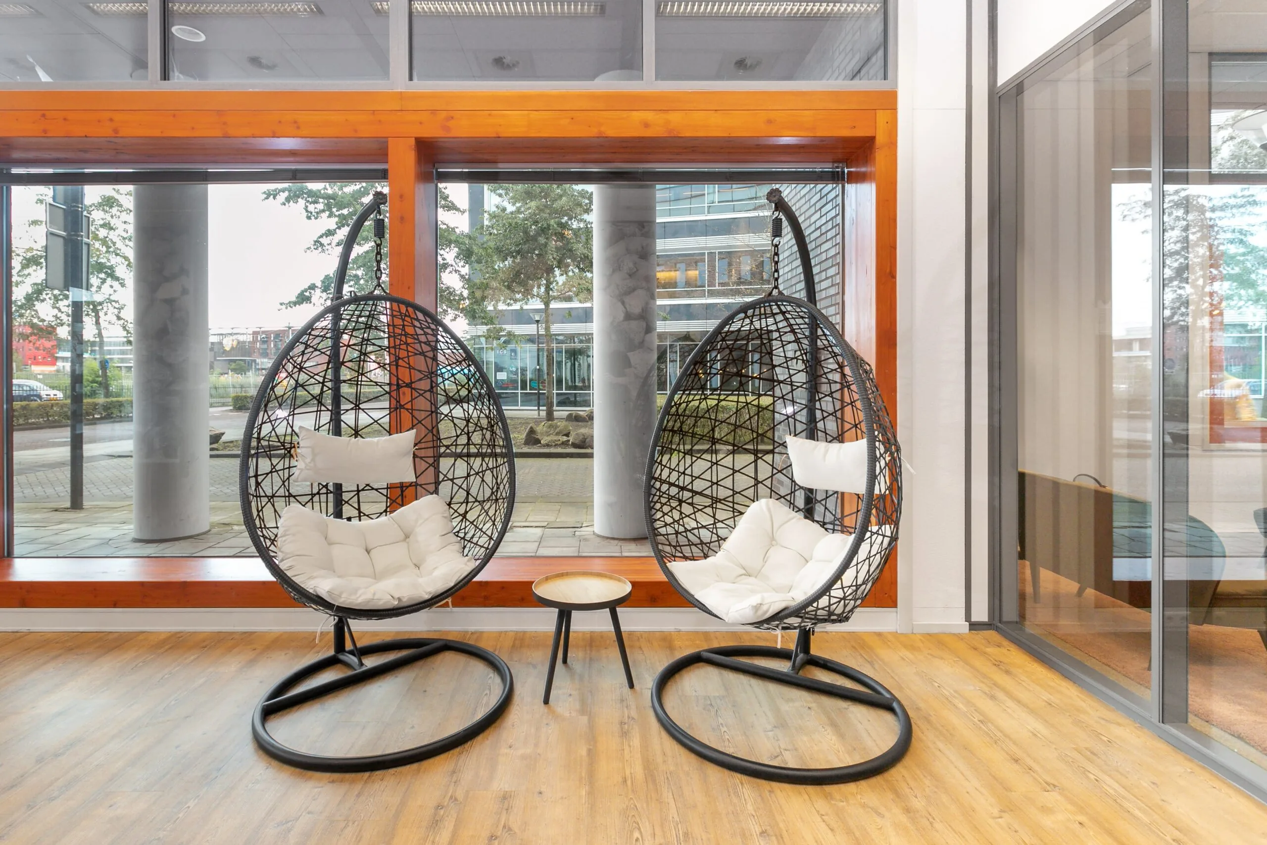 Moderne wachtruimte in een kantoorpand aan het Smallepad 32 in Amersfoort met twee hangstoelen en een klein tafeltje bij grote ramen.