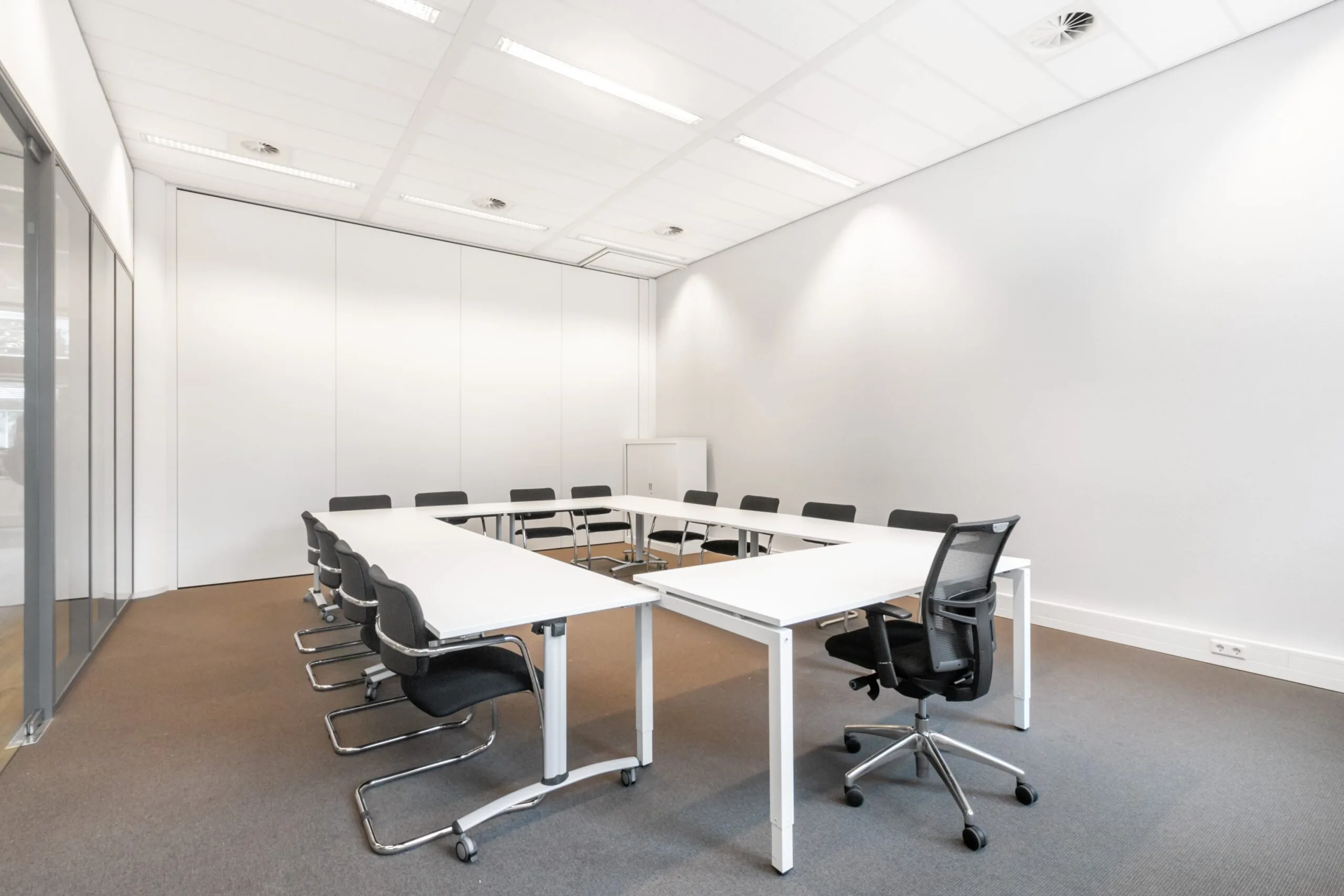 Lichte vergaderruimte met U-vormige opstelling van witte tafels en zwarte stoelen in kantoor aan Smallepad 32 in Amersfoort.