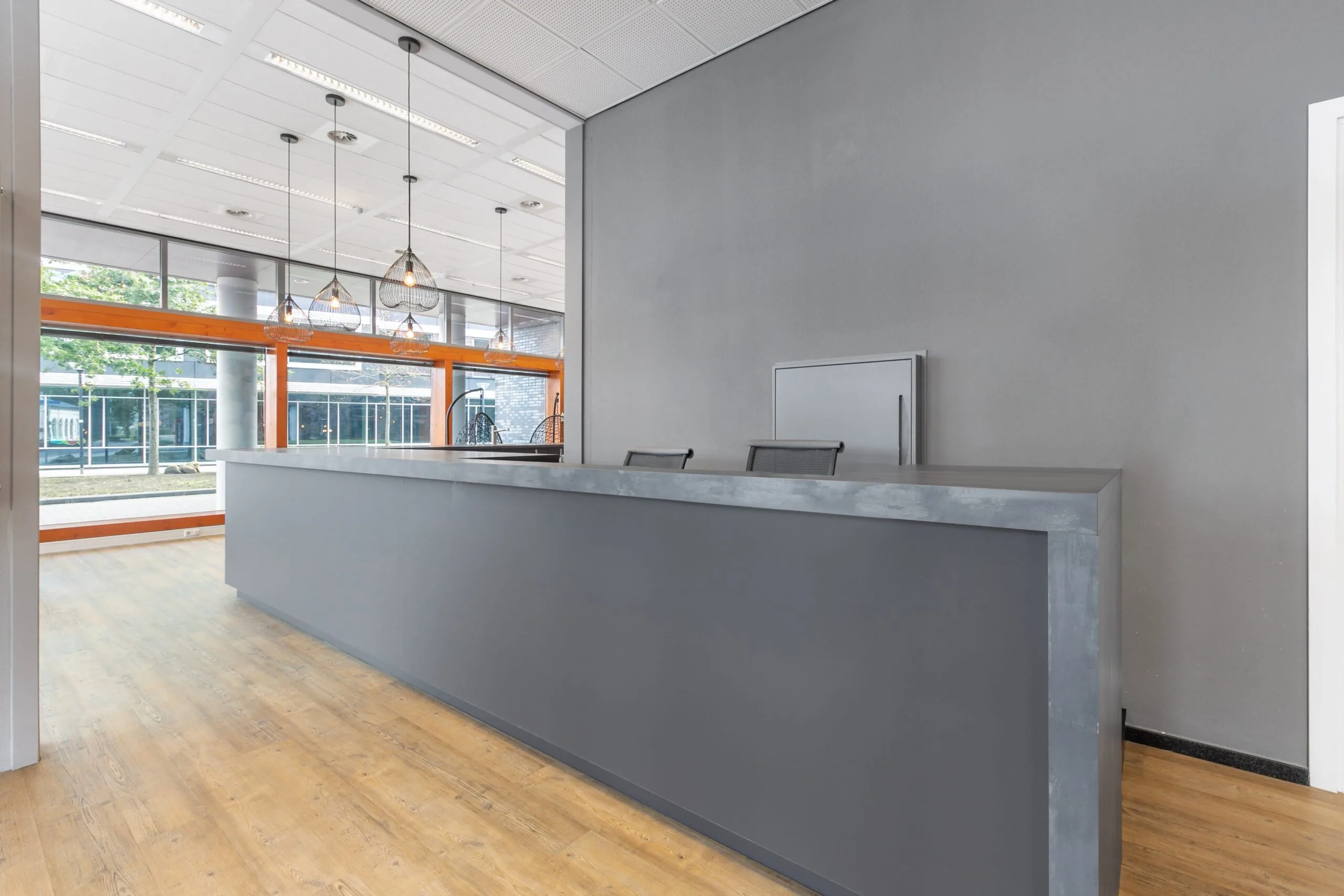 Moderne ontvangstruimte met grijze balie, houten vloer en grote ramen in een kantoorpand aan het Smallepad 32 in Amersfoort.