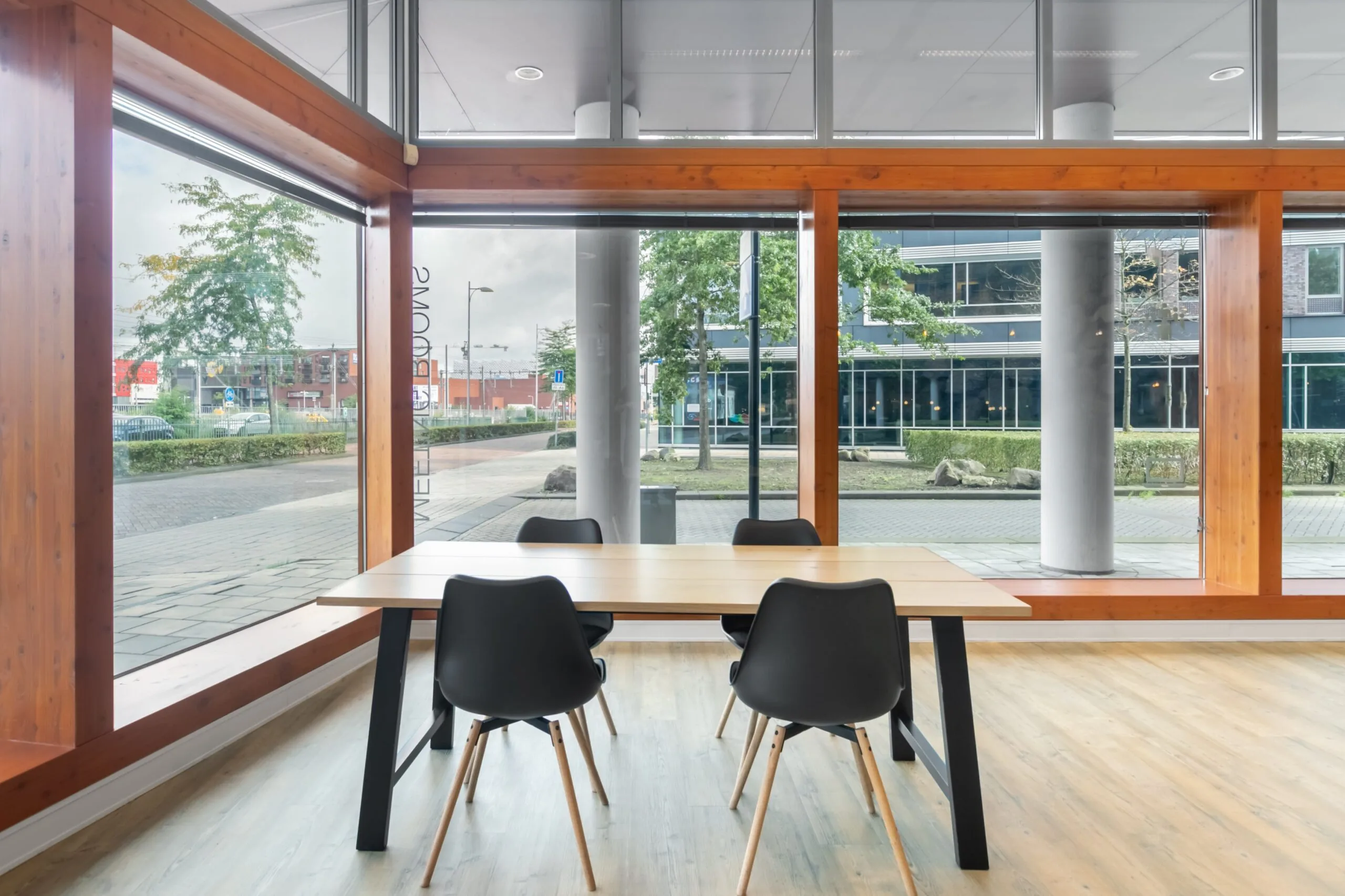 Moderne kantoorruimte met grote ramen, een houten vergadertafel en vier zwarte stoelen aan het Smallepad 32 in Amersfoort.