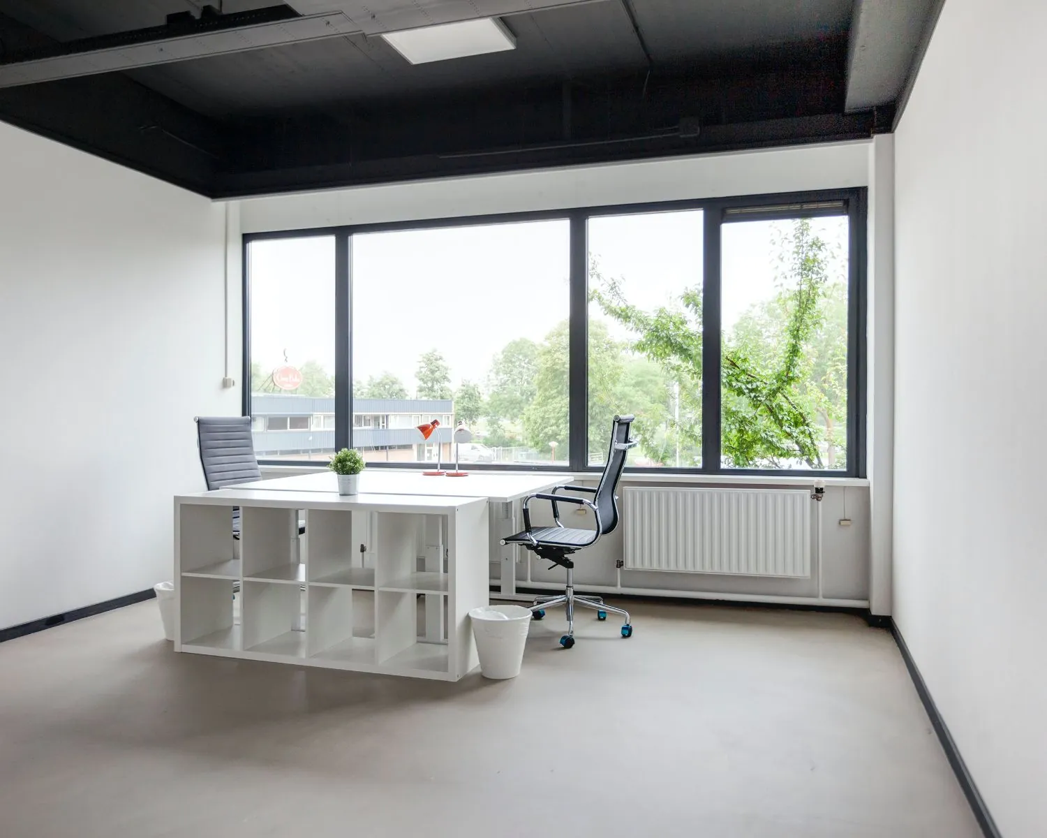 Moderne, lichte kantoorruimte met groot raam, twee bureaustoelen en een wit bureau aan de Tarasconweg 2 in Eindhoven.