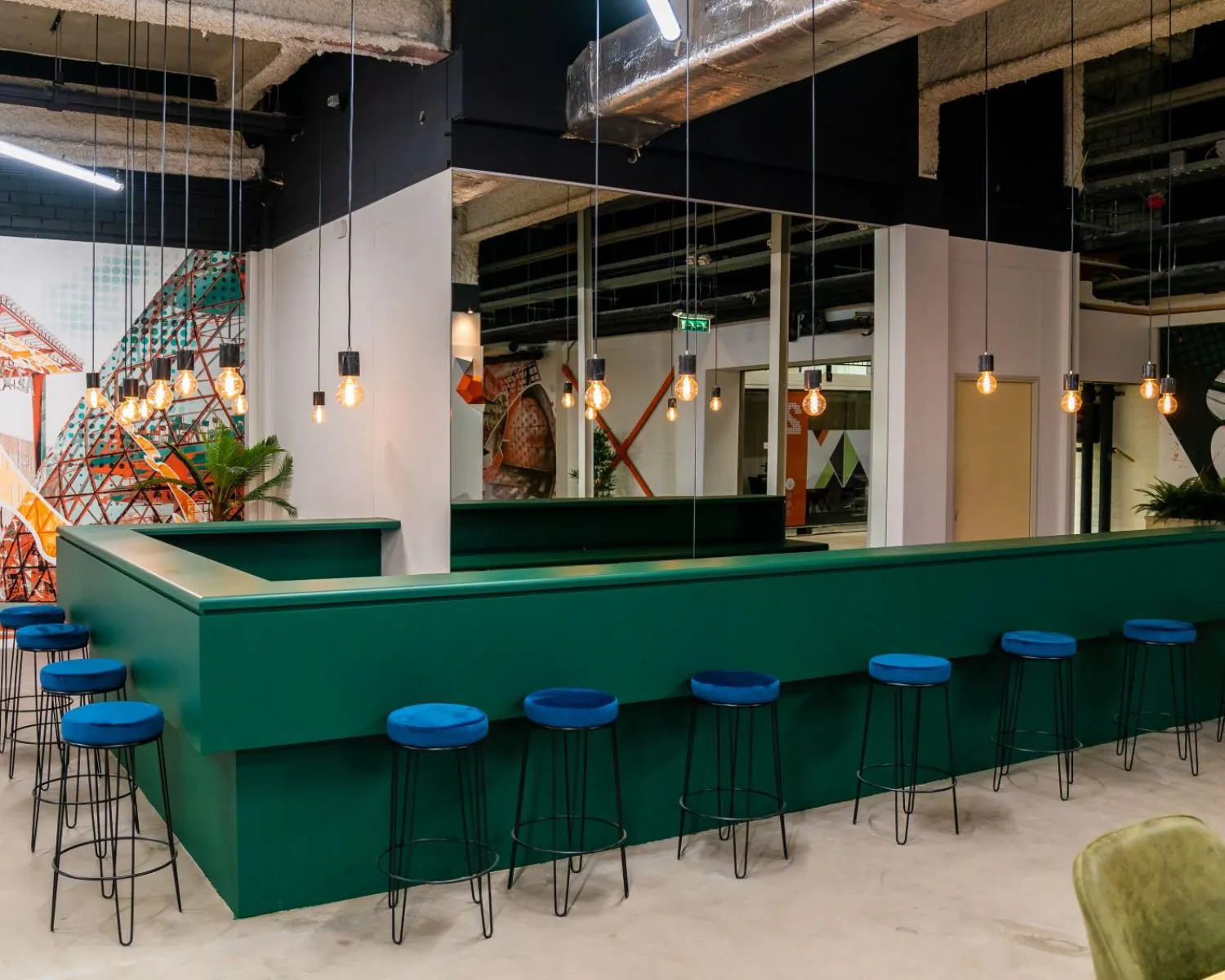 Moderne kantoorruimte aan de Tarasconweg 2 in Eindhoven met een groene bar, blauwe barkrukken en industriële verlichting.