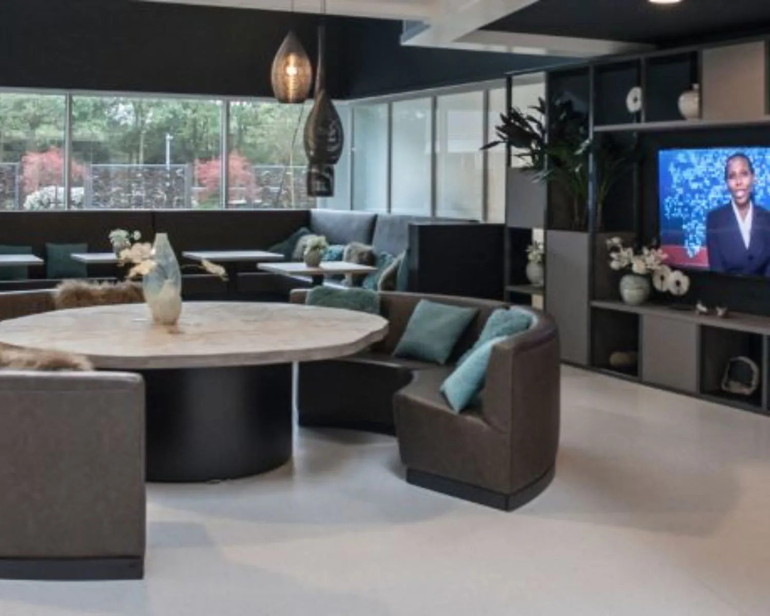 Moderne lounge- en wachtruimte in een kantoor aan de Thomas R. Malthuslaan 1 in Amsterdam, met ronde zitbanken, een grote tafel en een televisiescherm aan de muur.