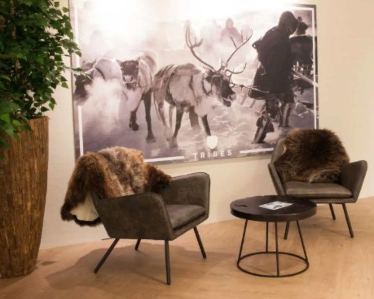 Sfeervolle wachtruimte met twee stoelen met bontkleden, een ronde tafel en een grote wandfoto bij Tribes-kantoor aan de Thomas R. Malthuslaan in Amsterdam.