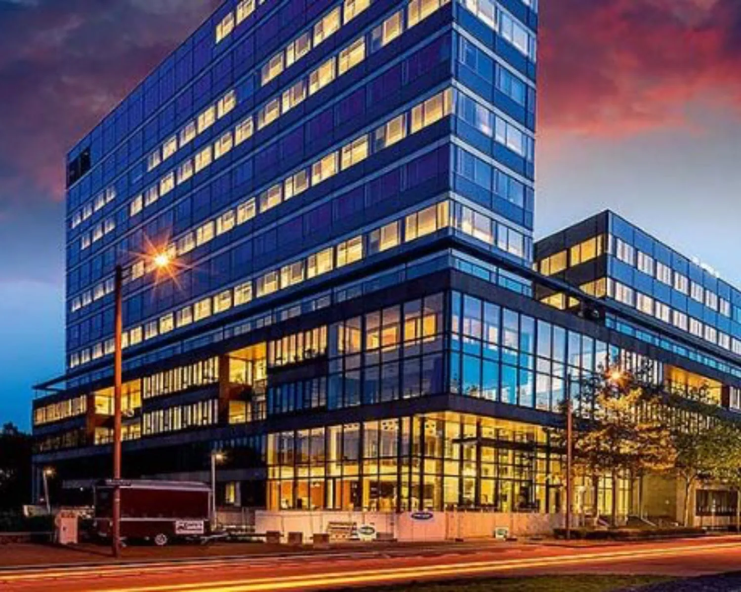 Modern kantoorgebouw aan de Thomas R. Malthuslaan 1 in Amsterdam, verlicht tijdens de avondschemering.