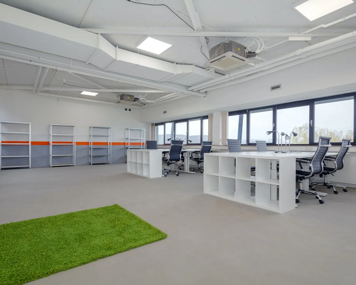 Moderne, lichte kantoorruimte met bureaus, bureaustoelen, open kasten en een groen vloerkleed aan de Transistorstraat 151 in Almere.