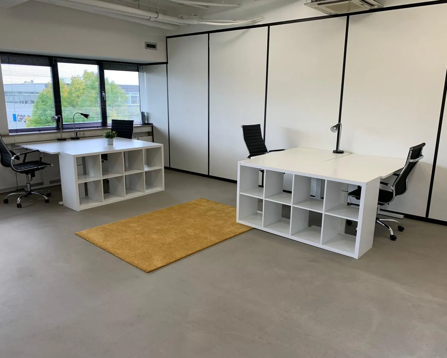 Moderne kantoorruimte met drie werkplekken, witte bureaus met opbergruimte, zwarte bureaustoelen en een geel vloerkleed bij Transistorstraat 151 in Almere.