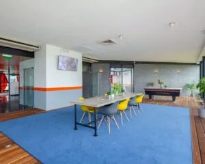Moderne kantoorruimte aan de Transistorstraat 151 in Almere met vergadertafel, kleurrijke stoelen, pooltafel en planten op een blauwe vloerbedekking.
