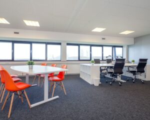 Moderne kantoorruimte met witte bureaus, oranje stoelen en grote ramen aan de Transistorstraat 151 in Almere.