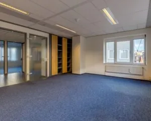 Lichte en nette kantoorruimte met blauw tapijt, ingebouwde kasten en glazen deuren aan de Vossenstraat 6.