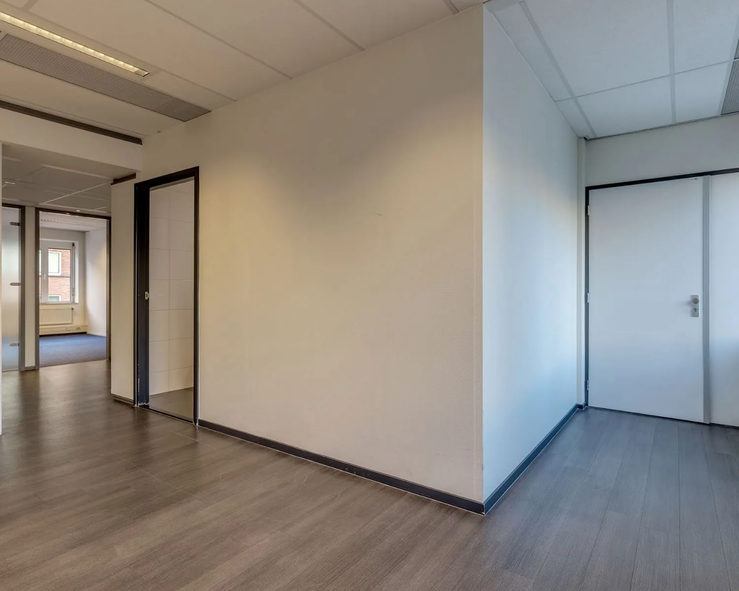 Moderne kantoorruimte met witgrijze muren, donker laminaat en meerdere toegangsdeuren in Vossenstraat 6-3.