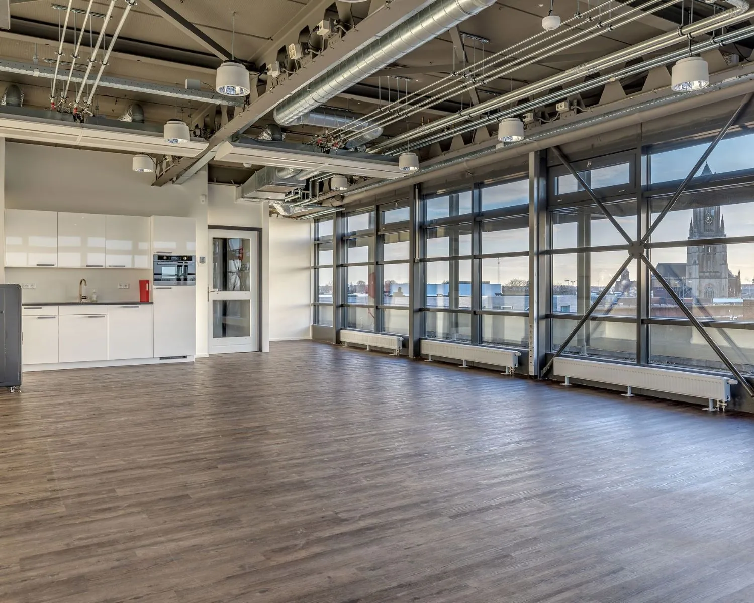 Moderne, open kantoorruimte met kitchenette en grote ramen aan de Vossenstraat 6-7 met uitzicht op de stad.