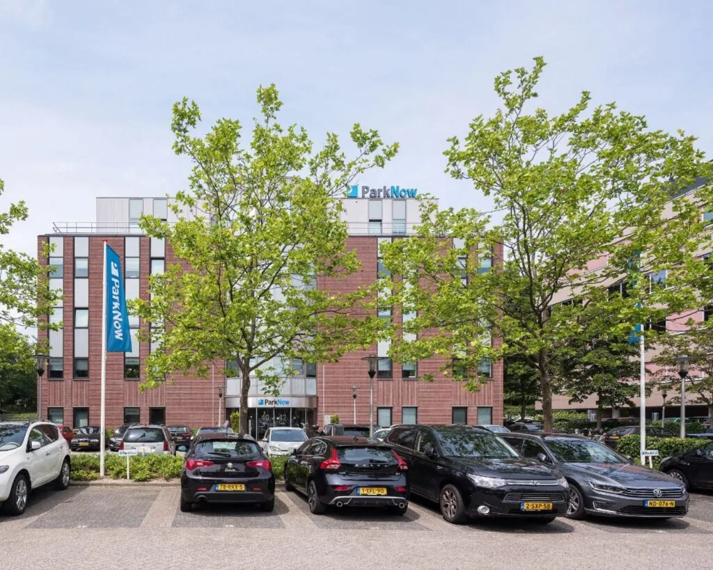Voorgevel van het kantoorgebouw Wisselwerking 40-48 met ParkNow-borden en geparkeerde auto's op de parkeerplaats.
