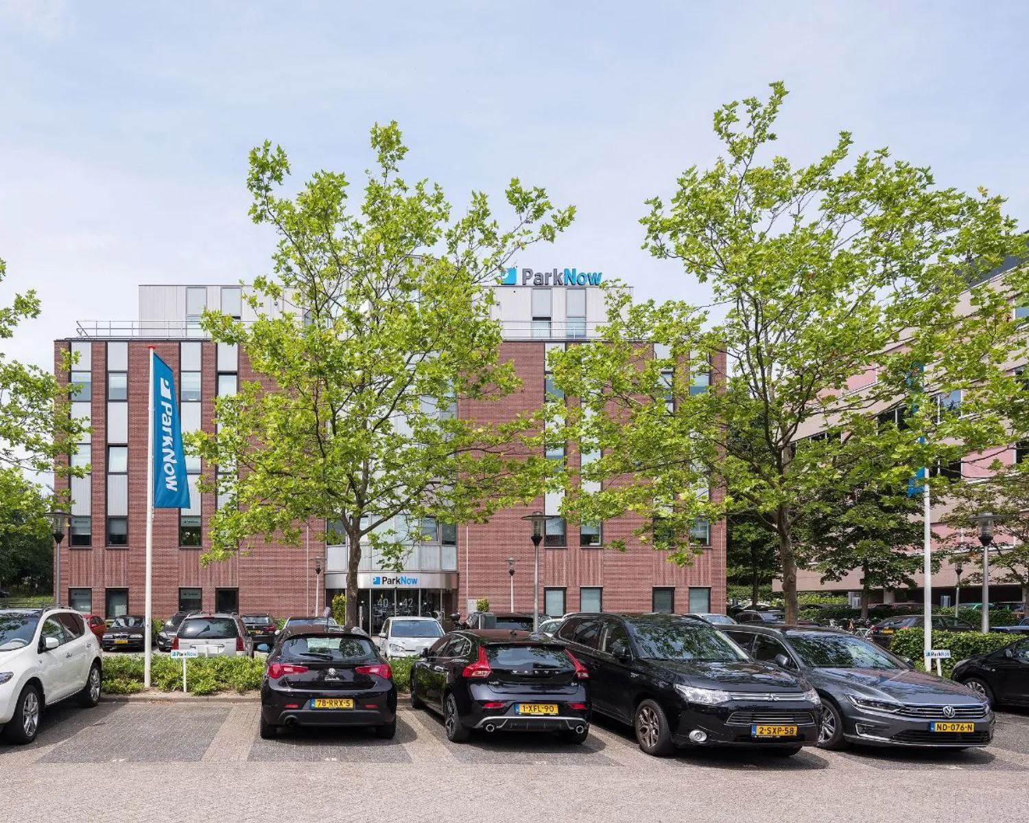 Voorgevel van het kantoorgebouw Wisselwerking 40-48 met ParkNow-borden en geparkeerde auto's op de parkeerplaats.