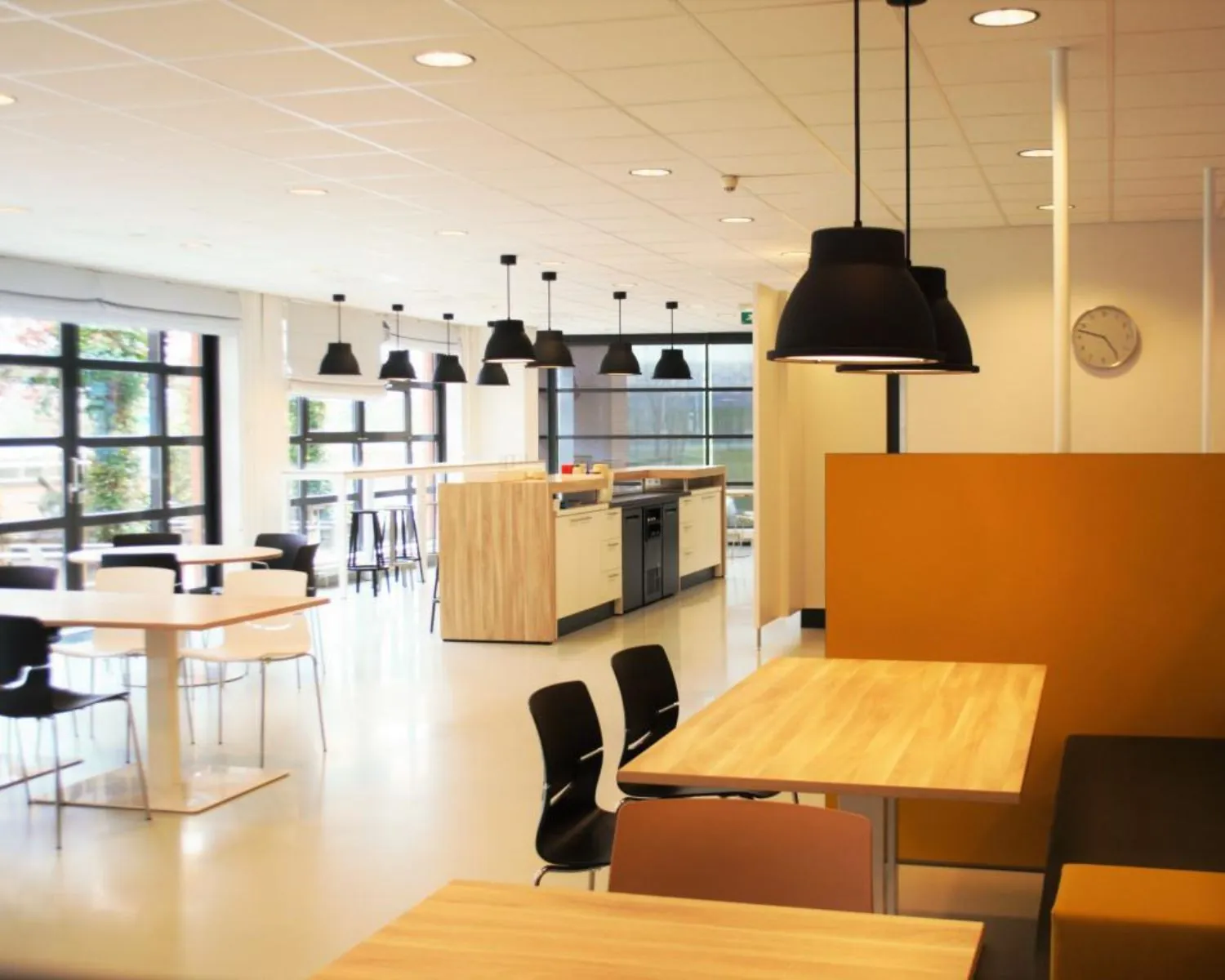 Moderne kantine in een kantoorpand aan de Zonnebaan 8 in Utrecht met houten tafels, designstoelen en grote ramen.