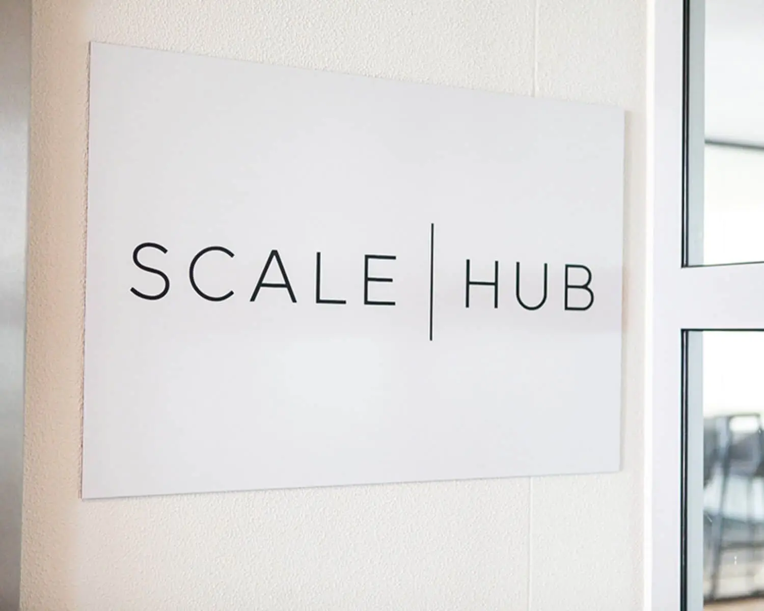 Wit naambord met het logo van SCALE | HUB bij de entree van een kantoorruimte in Amsterdam.