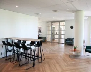 Moderne kantoorruimte in Amsterdam met hoge tafel, zitjes en glazen entreedeuren.