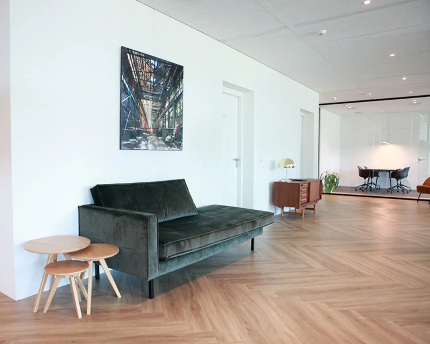 Moderne entree van een kantoorruimte in Amsterdam met een bank, bijzettafels en zicht op een vergaderruimte.