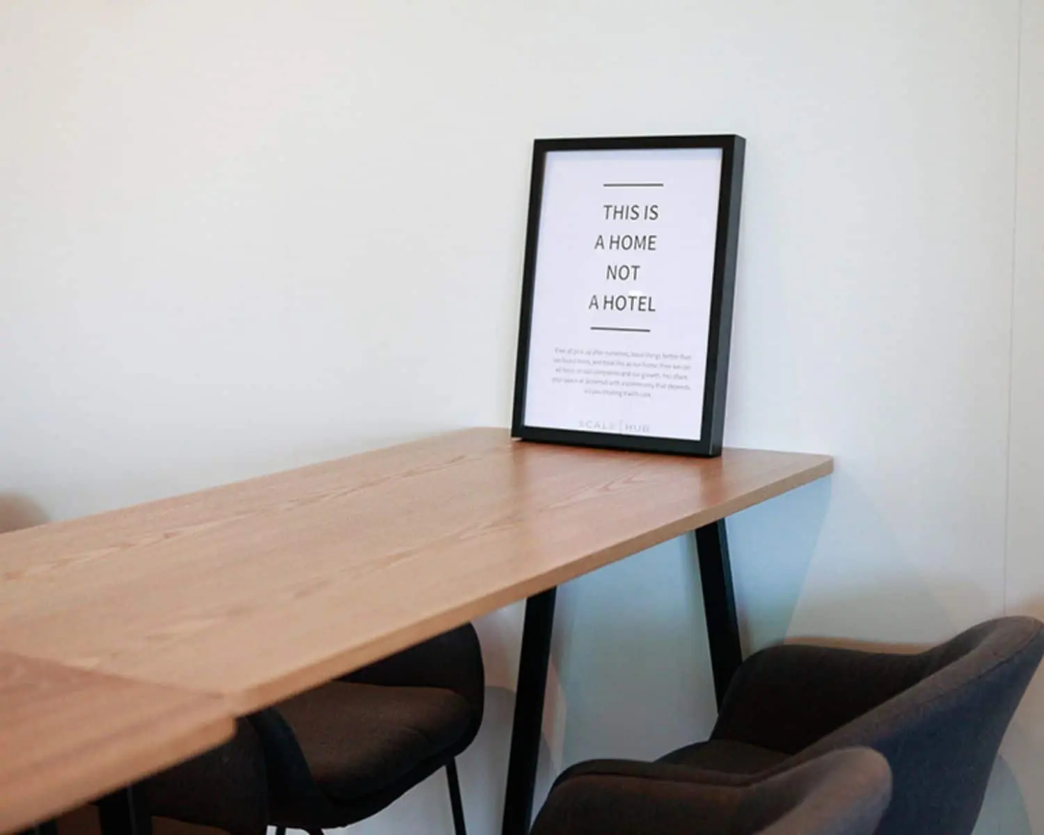Moderne kantoorruimte met houten vergadertafel, zwarte stoelen en een ingelijst citaat tegen een witte muur.