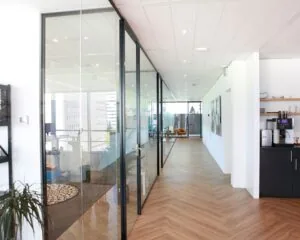 Moderne kantoorruimte in Amsterdam met glazen vergaderruimtes, houten visgraatvloer en een koffiecorner.