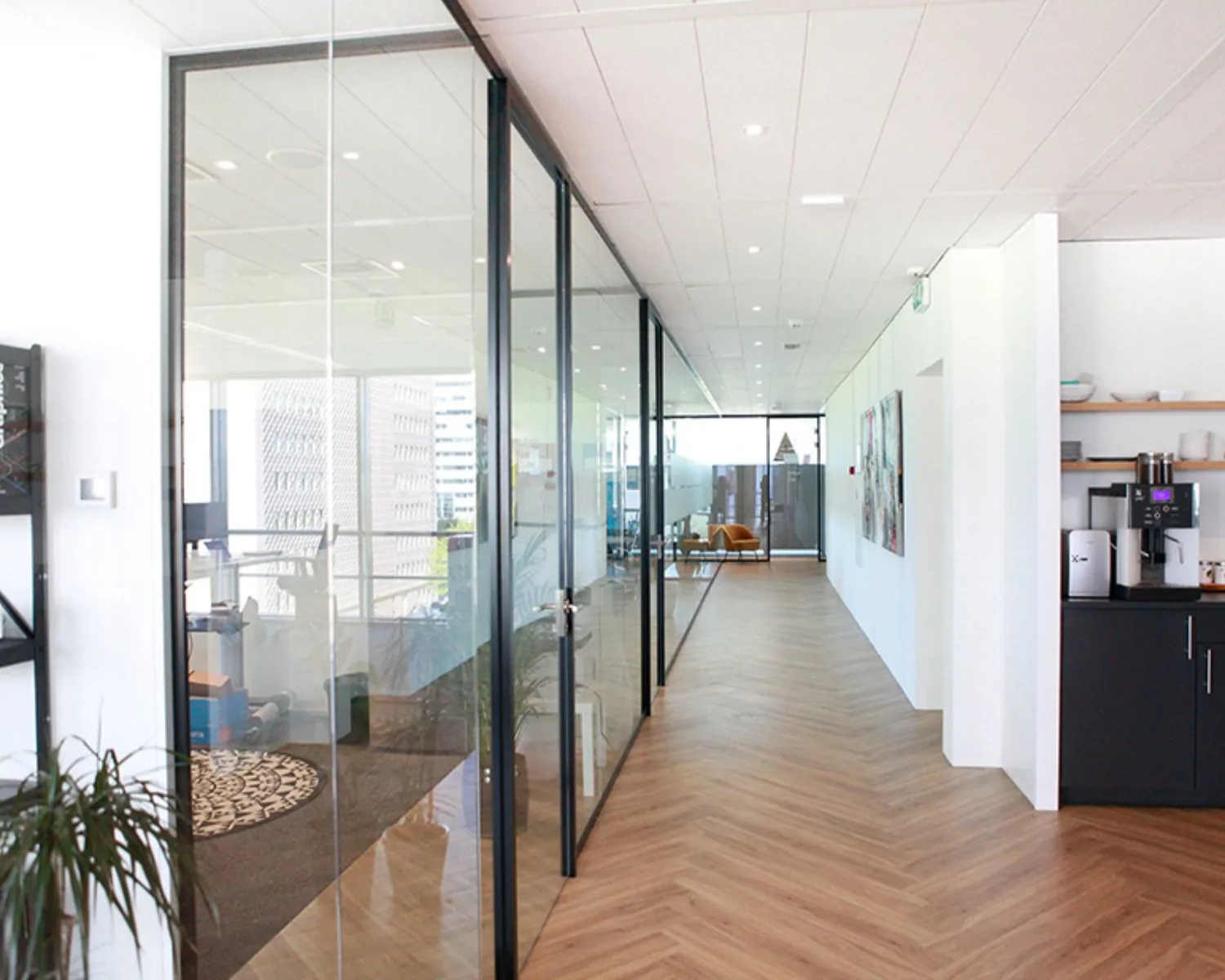 Moderne kantoorruimte in Amsterdam met glazen vergaderruimtes, houten visgraatvloer en een koffiecorner.