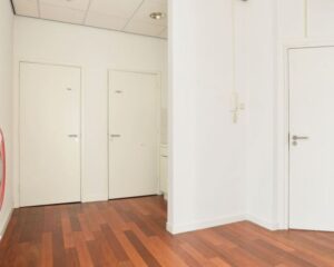 Witte hal met houten vloer en meerdere gesloten deuren in een kantoorruimte aan het Houtplein 22 in Haarlem.