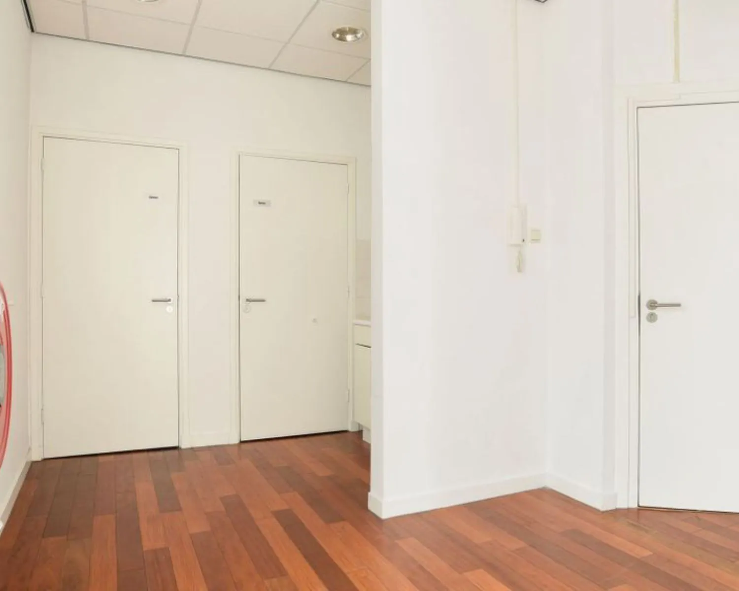 Witte hal met houten vloer en meerdere gesloten deuren in een kantoorruimte aan het Houtplein 22 in Haarlem.
