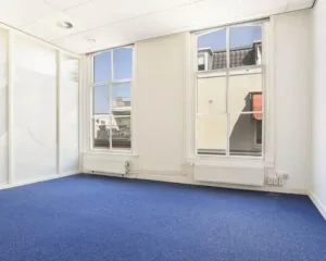 Lichte kantoorruimte met blauwe vloerbedekking en grote ramen aan het Houtplein 22 in Haarlem.