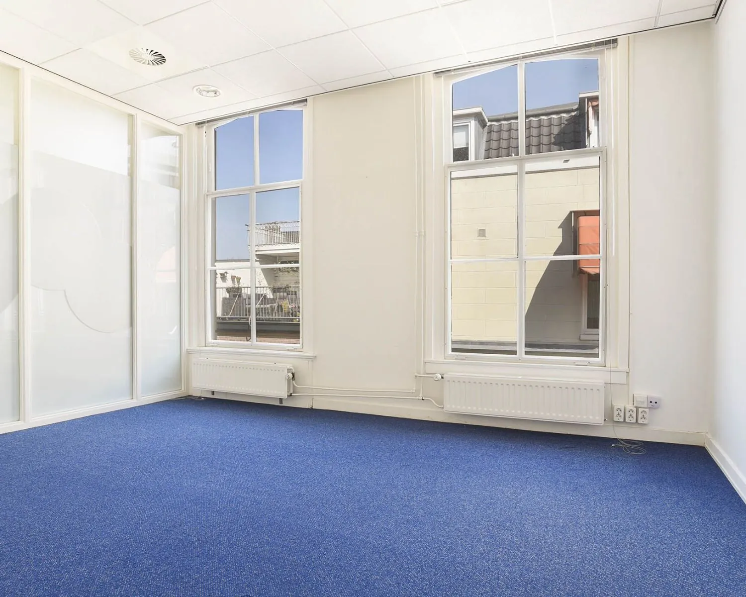 Lichte kantoorruimte met blauwe vloerbedekking en grote ramen aan het Houtplein 22 in Haarlem.