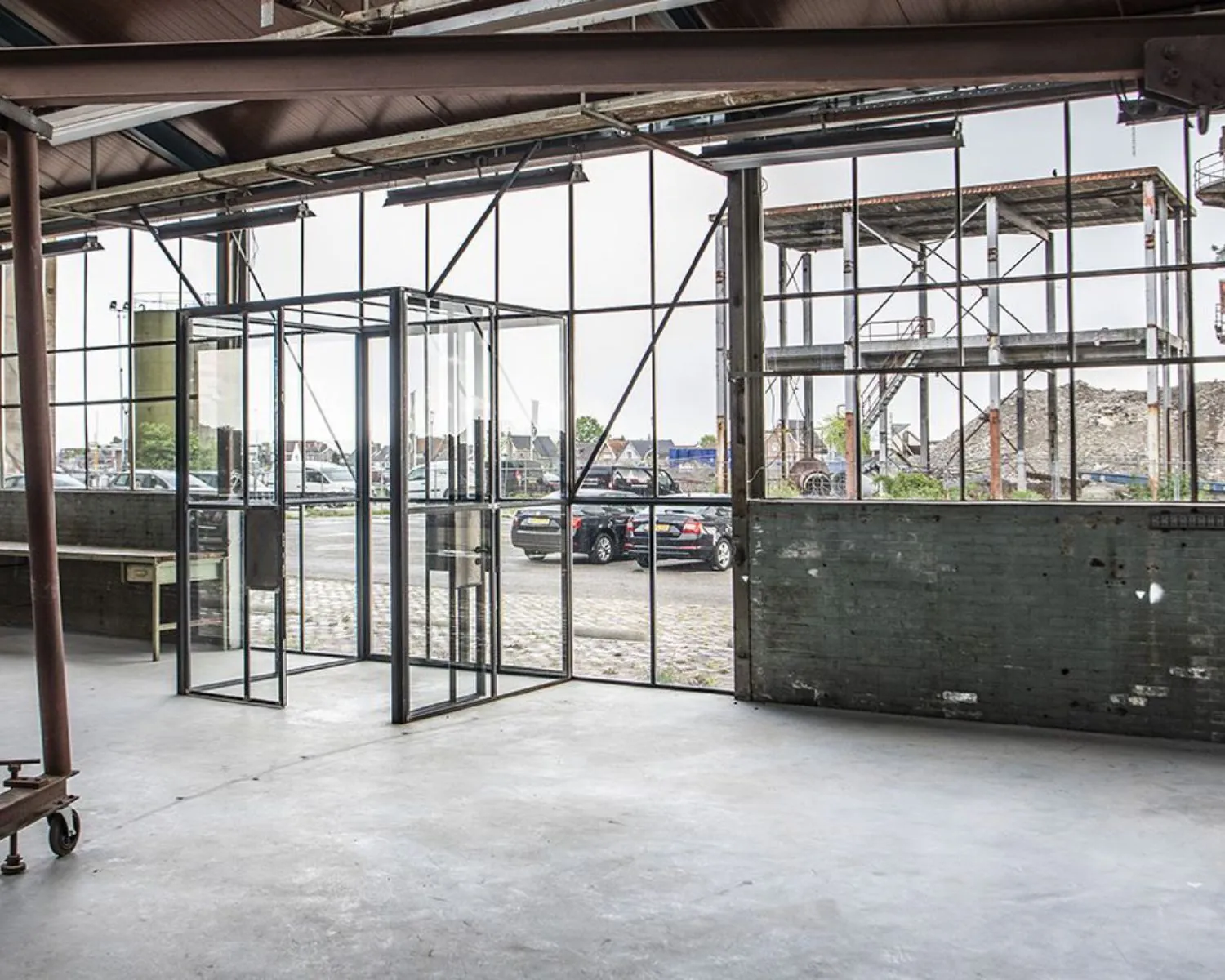 Industriële kantoorruimte met glazen entree en uitzicht op parkeerplaats en bouwconstructie aan het Kalkhovenplein 3b in Halfweg.