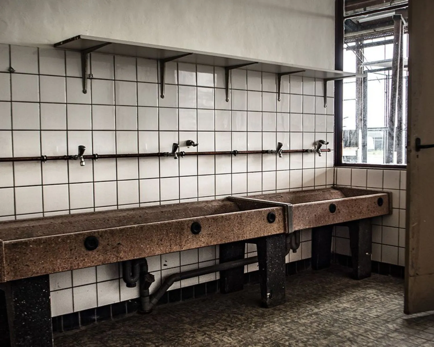 Oude wasruimte met meerdere wastafels en wandkranen in een kantoorruimte aan het Kalkhovenplein 3b in Halfweg.