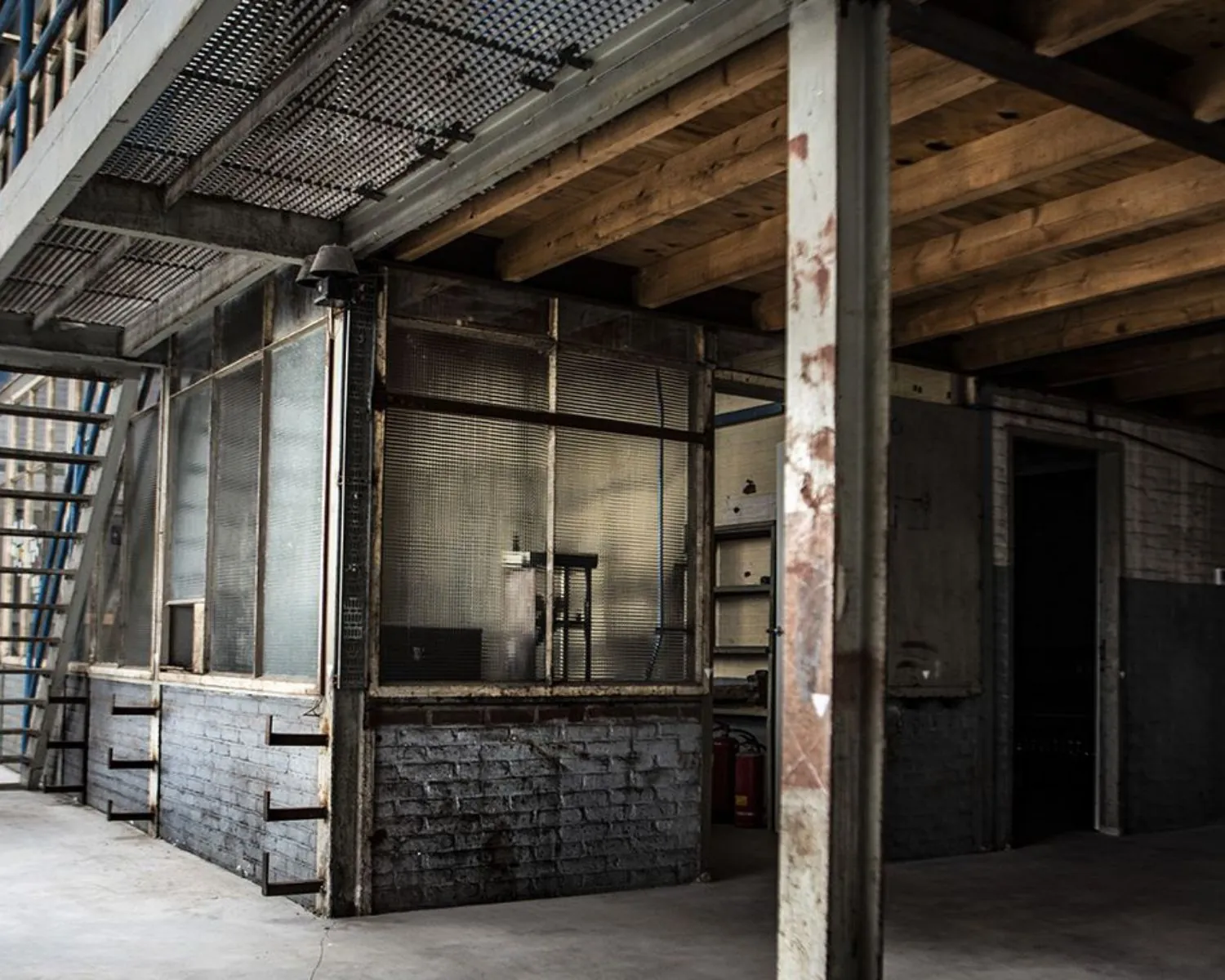 Industrieel ogende kantoorruimte met metalen trap, houten plafondbalken en glazen scheidingswanden aan het Kalkhovenplein 3b in Halfweg.