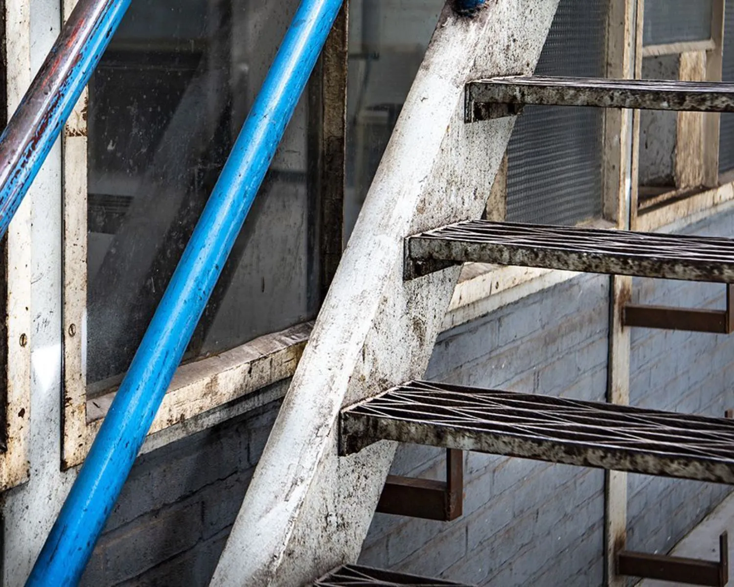 Buitentrap van metaal met blauwe en witte leuningen aan een verweerd kantoorgebouw op het Kalkhovenplein 3b in Halfweg.