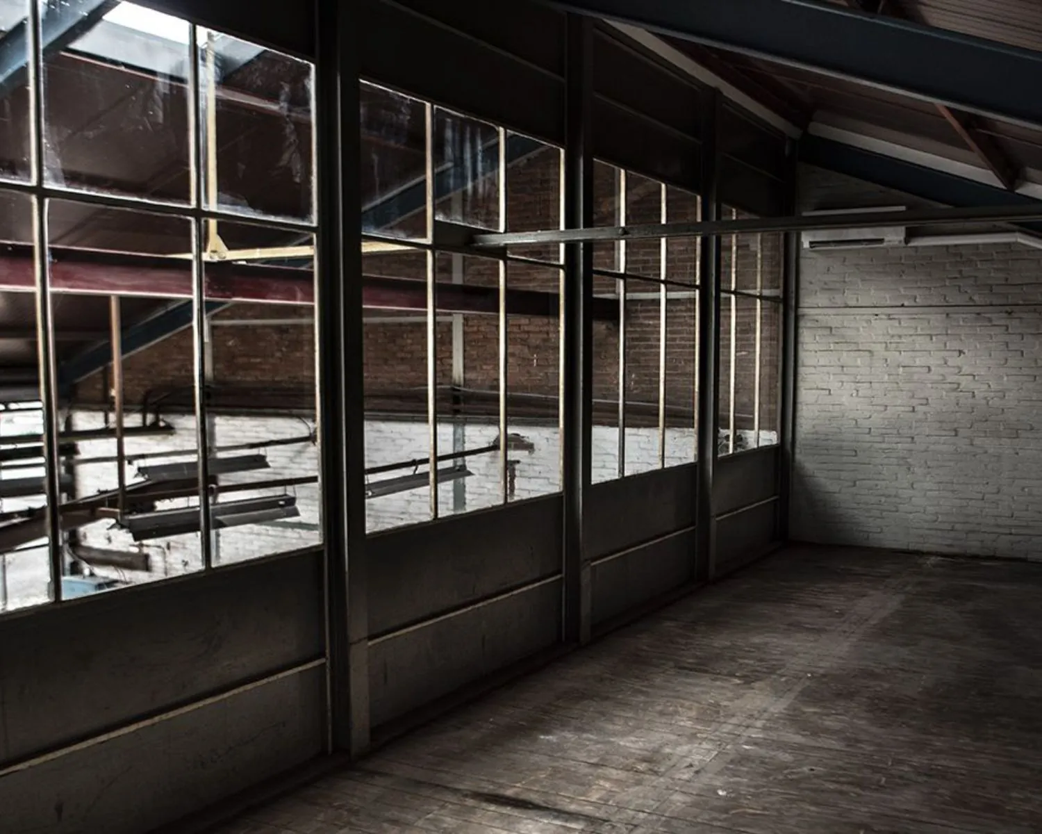 Lege, industriële kantoorruimte met houten vloer en grote ramen aan het Kalkhovenplein 3B in Halfweg.