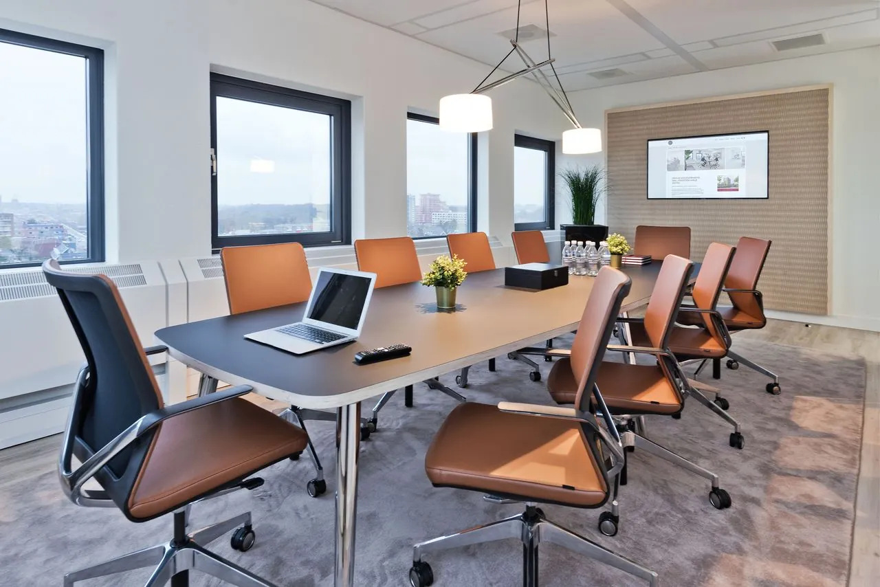 Moderne vergaderruimte in kantoorpand Kennemerhaghe aan de Leidsevaartweg 99 in Heemstede met grote tafel, leren stoelen en presentatiescherm.