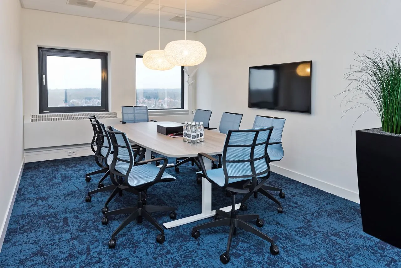 Moderne vergaderruimte met acht bureaustoelen, een houten tafel, flatscreen, en uitzicht in kantoorgebouw Kennemerhaghe in Heemstede.