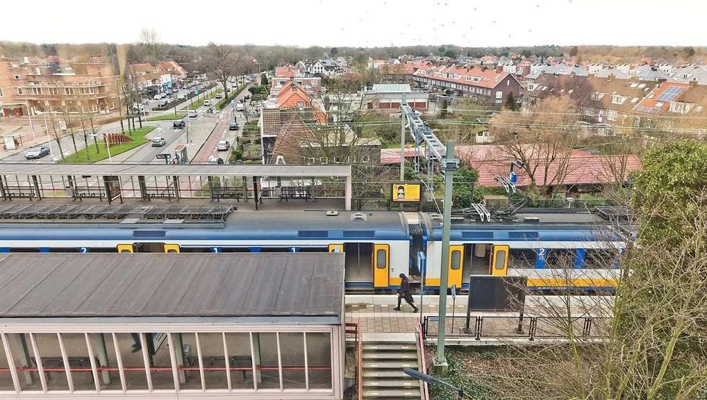Uitzicht op station Heemstede-Aerdenhout met een passerende trein en woonwijk op de achtergrond.