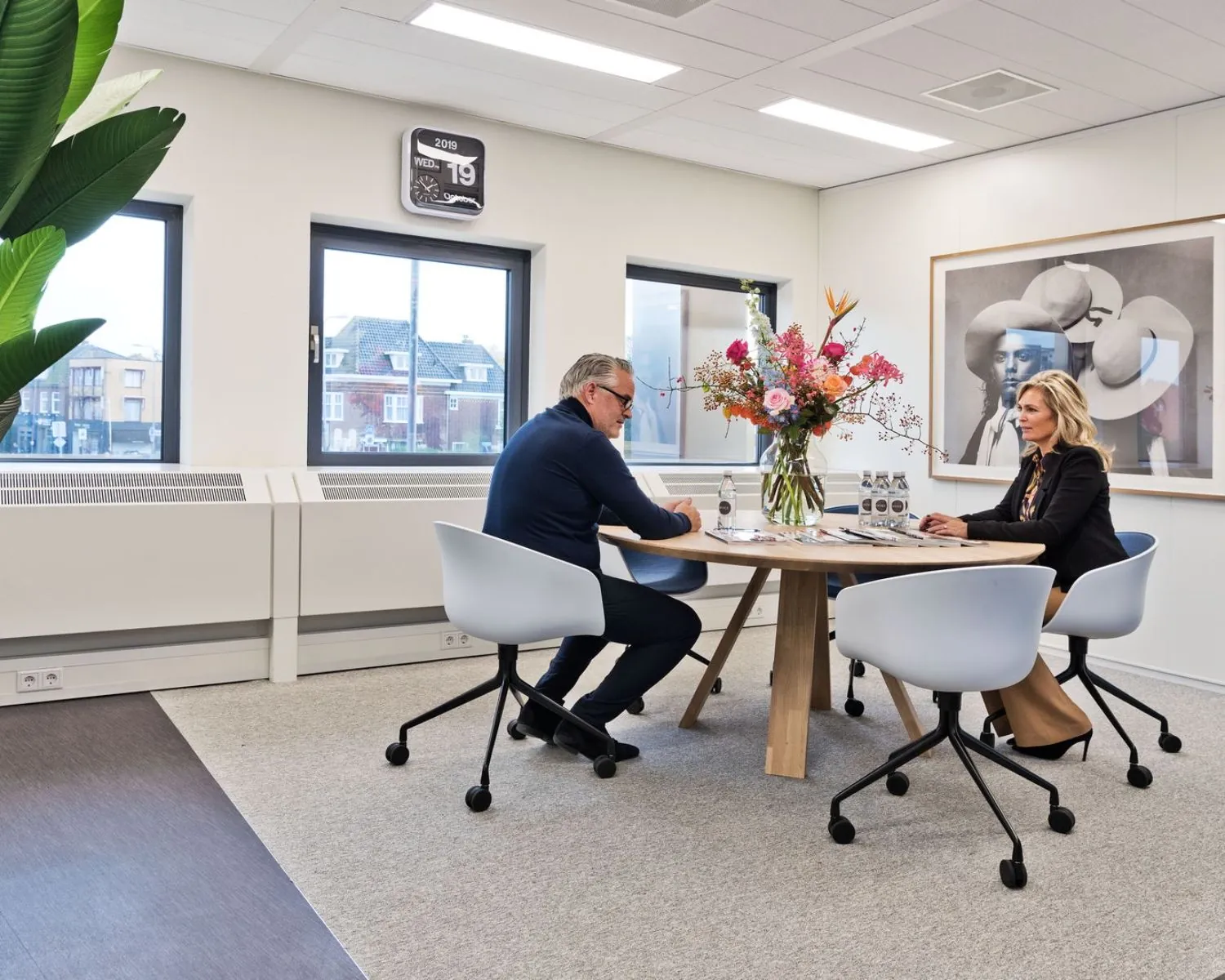 Twee personen zitten aan een ronde tafel in een moderne kantoorruimte in het gebouw Kennemerhaghe aan de Leidsevaartweg 99 in Heemstede.