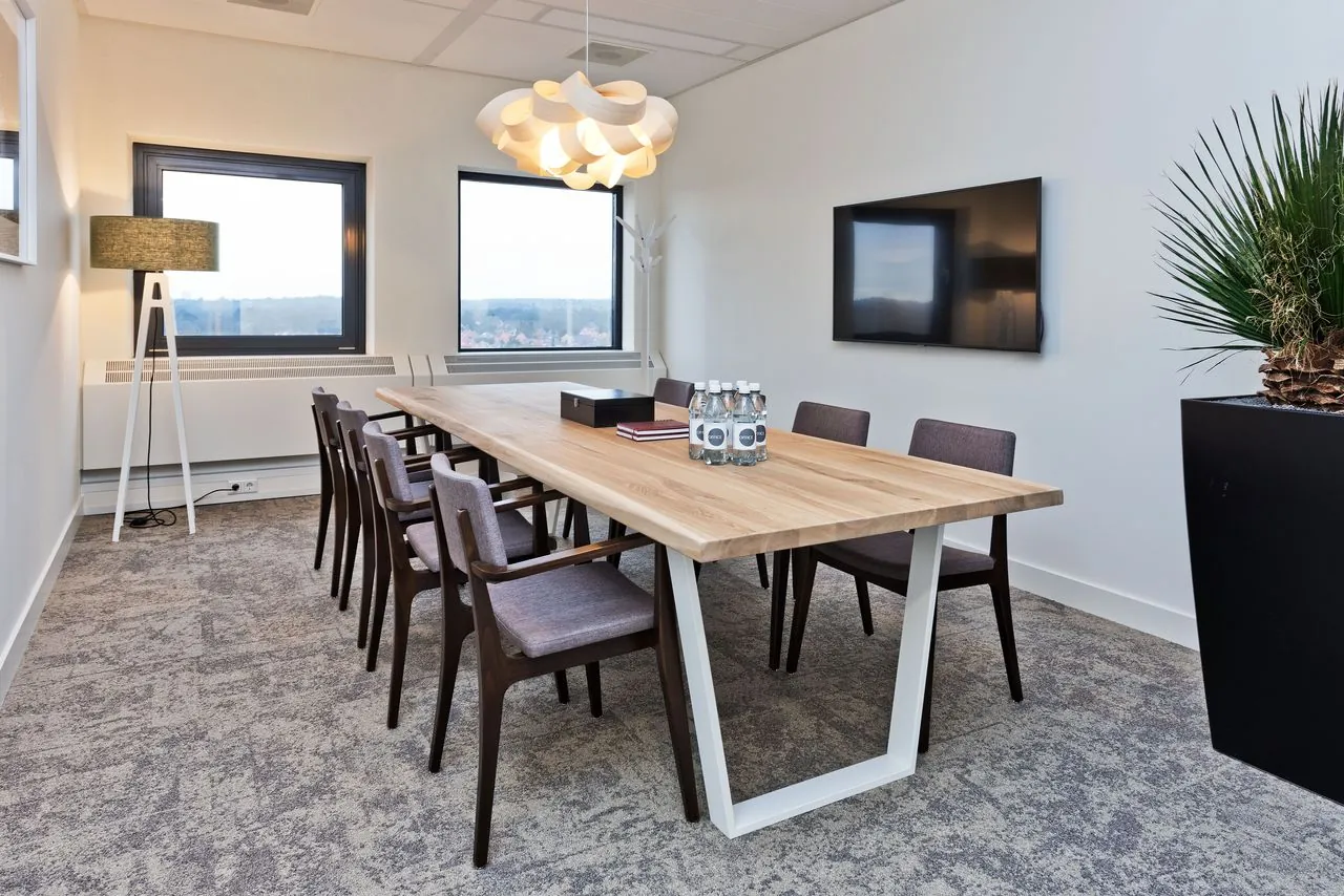 Moderne vergaderruimte in kantoorpand Kennemerhaghe in Heemstede met houten tafel, stoelen, designlamp en flatscreen.