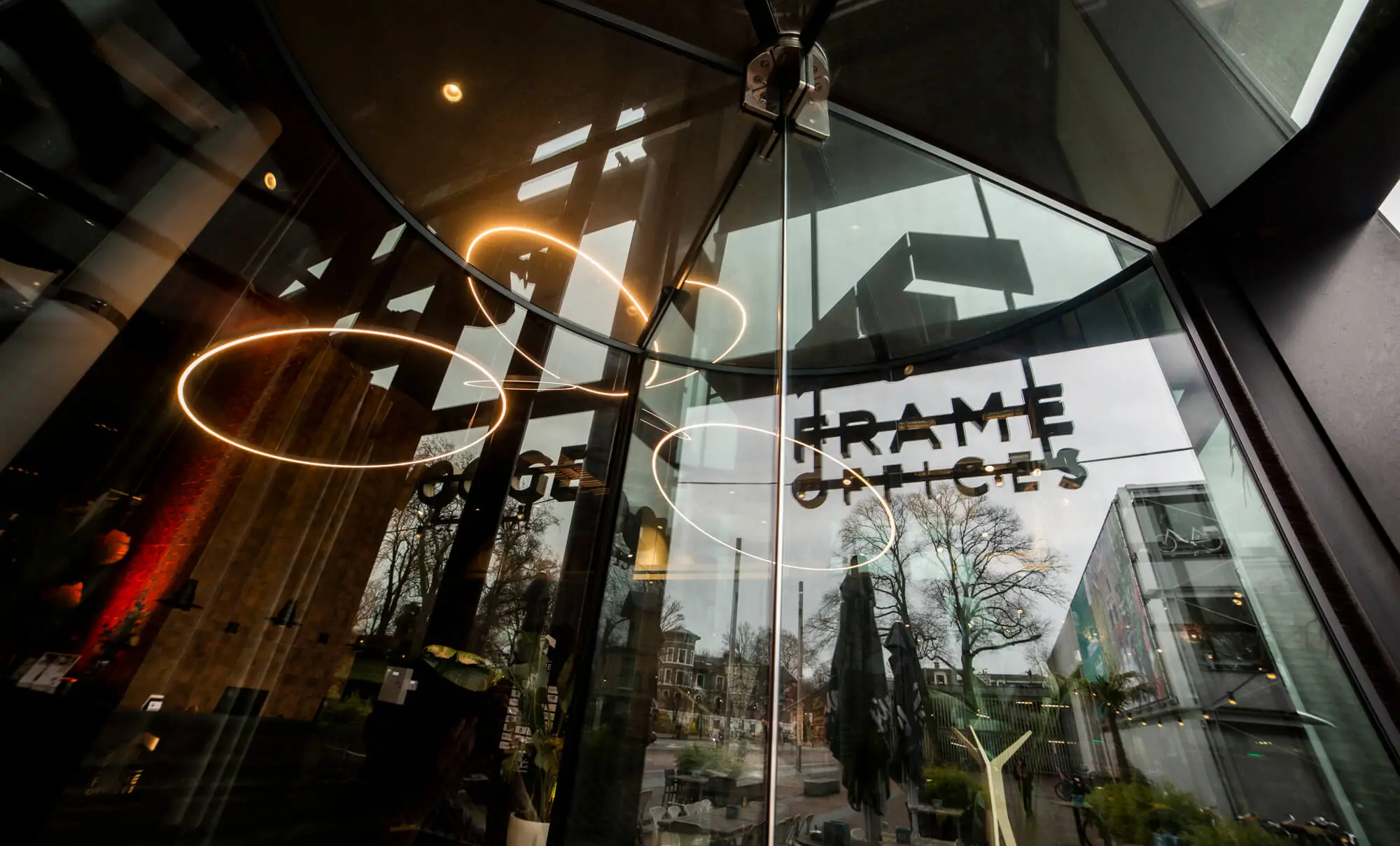 Moderne glazen entree van Frame Offices aan het Kennemerplein in Haarlem, met reflecties van de omgeving en sierlijke lichtarmaturen.