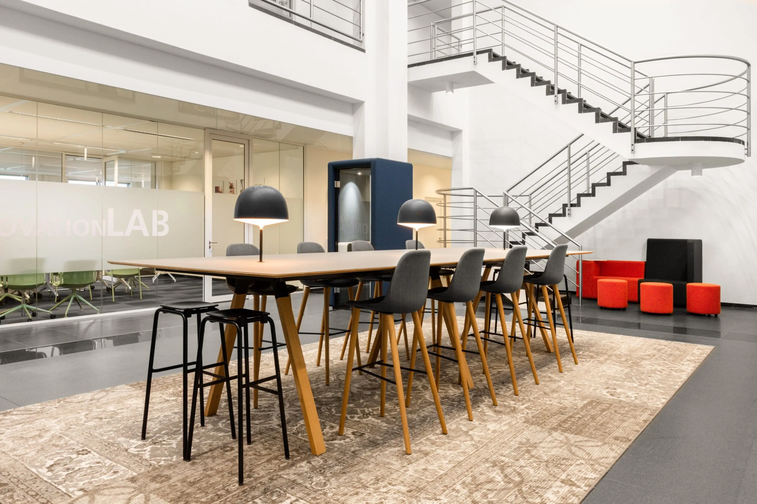 Moderne kantoorruimte aan de Laarderhoogtweg in Amsterdam met een lange vergadertafel, designlampen, glazen vergaderruimte en open trap.