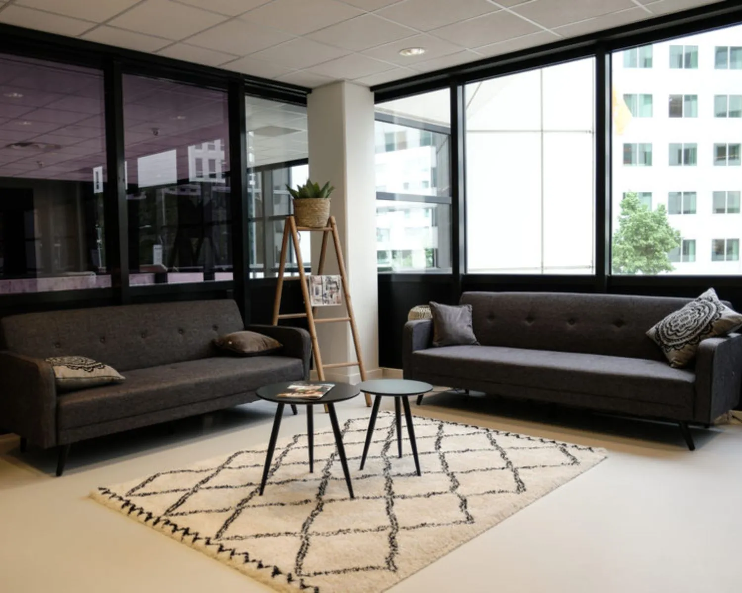 Moderne wachtruimte in een kantoor aan de Marten Meesweg in Rotterdam met twee grijze banken, een licht vloerkleed en grote ramen.