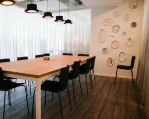 Vergaderruimte met lange houten tafel, zwarte stoelen, opvallende hanglampen en decoratieve borden aan de muur in kantoorpand aan de Marten Meesweg in Rotterdam.