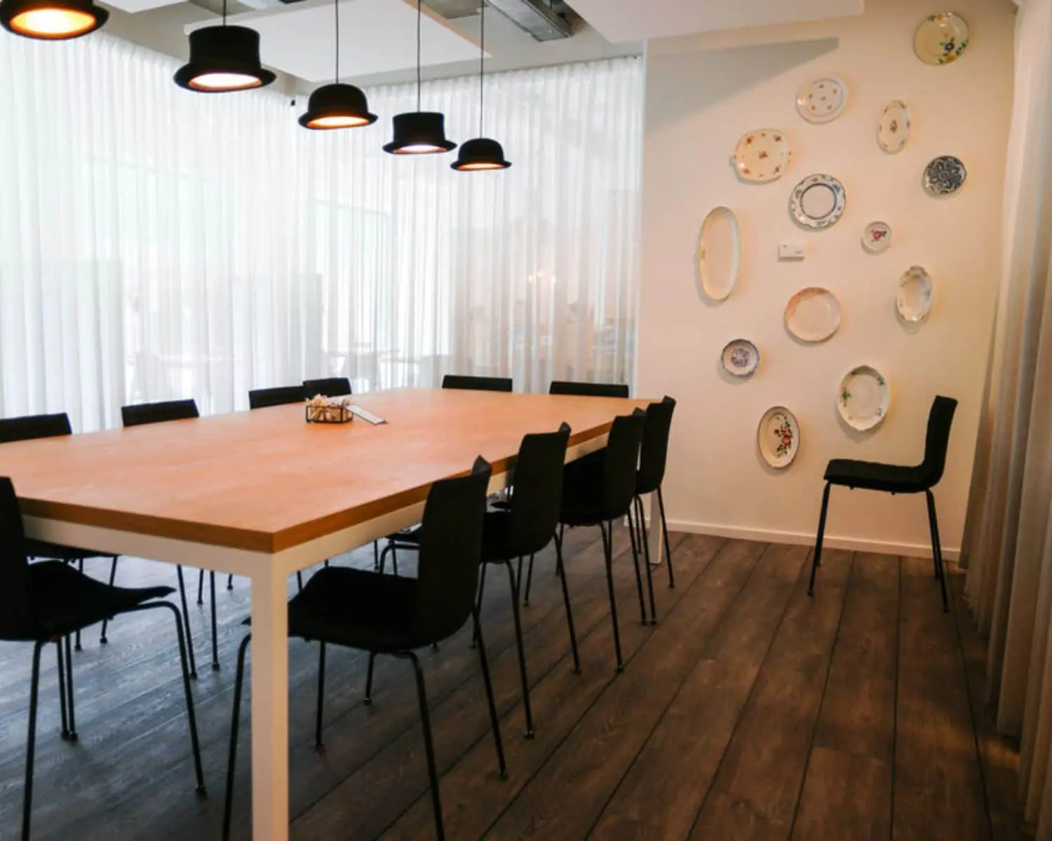 Vergaderruimte met lange houten tafel, zwarte stoelen, opvallende hanglampen en decoratieve borden aan de muur in kantoorpand aan de Marten Meesweg in Rotterdam.