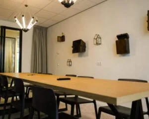 Vergaderruimte in een kantoor aan de Marten Meesweg in Rotterdam met een lange houten tafel, zwarte stoelen en decoratieve wandobjecten.