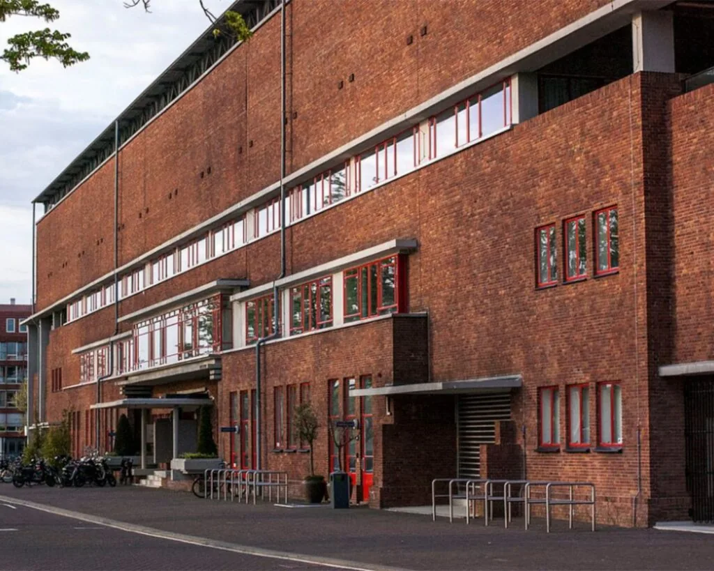 Bakstenen kantoorgebouw bij het Olympisch Stadion in Amsterdam met rode raamkozijnen en fietsenrekken voor de ingang.