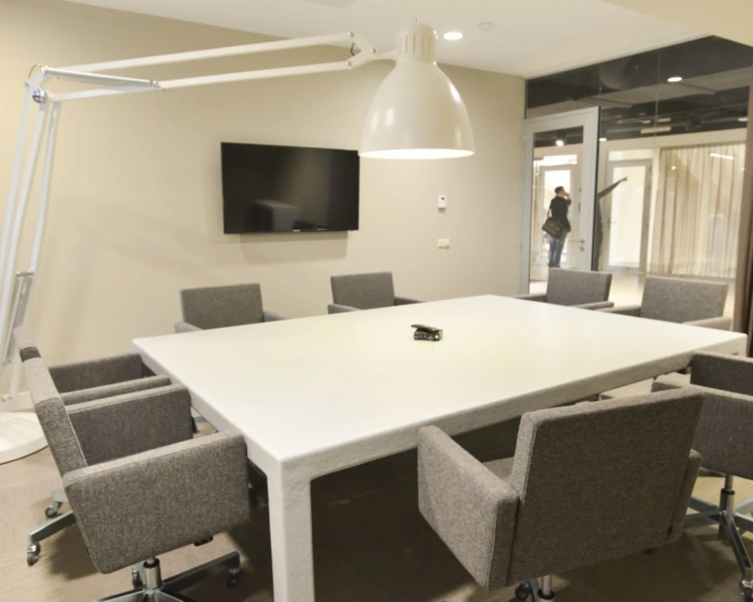 Vergaderruimte met modern wit tafelblad, grijze bureaustoelen, grote hanglamp en flatscreen in kantoorruimte bij het Olympisch Stadion in Amsterdam.