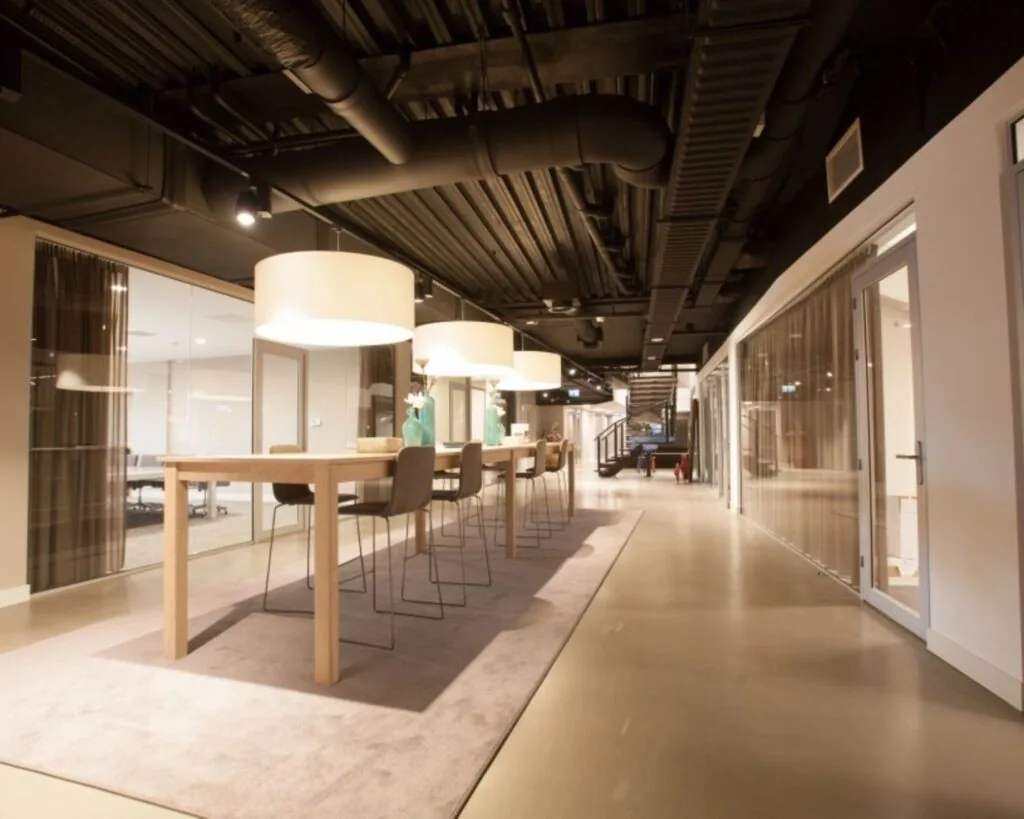 Moderne kantoorruimte te huur in het Olympisch Stadion in Amsterdam met lange houten vergadertafel en glazen wanden.