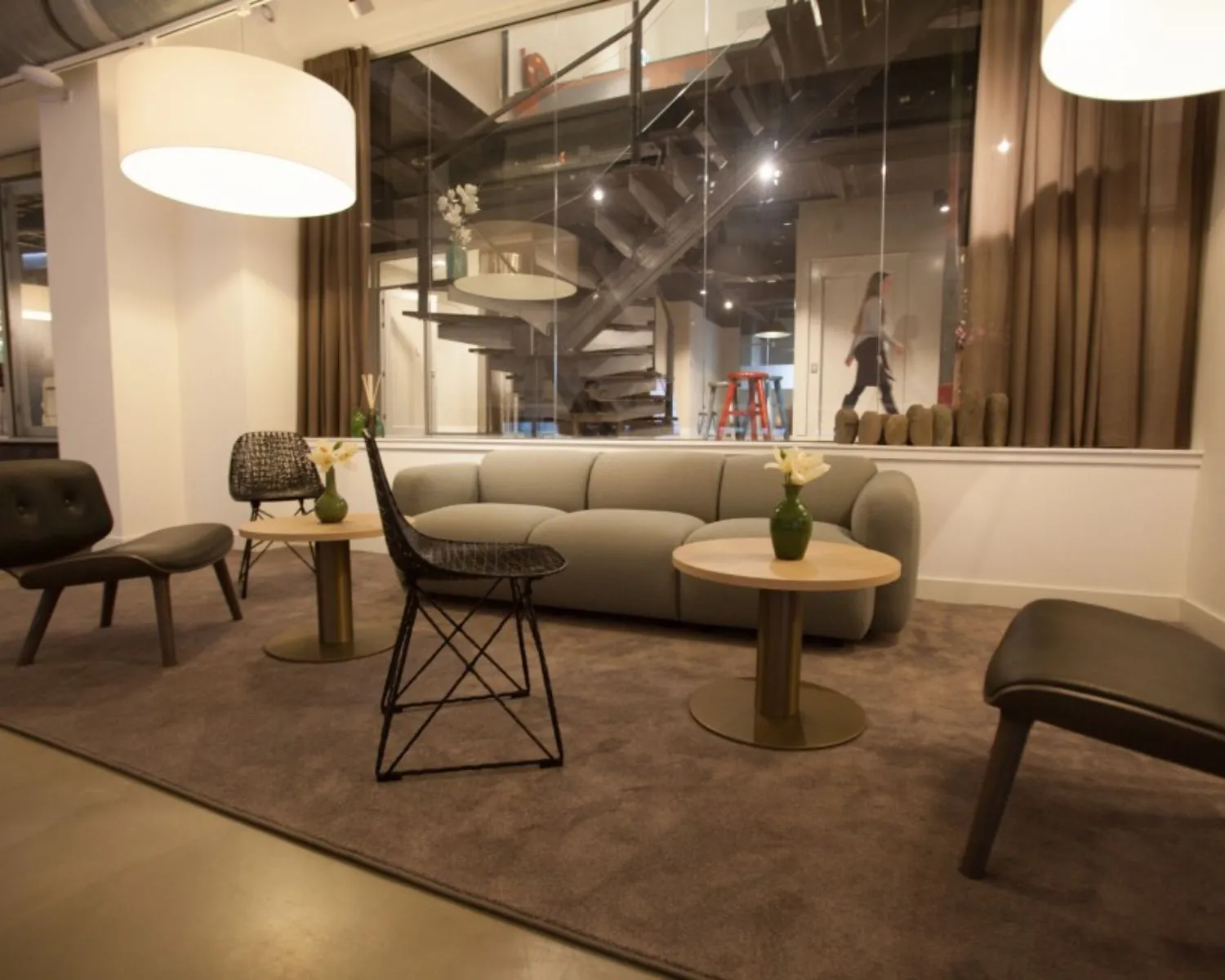 Moderne kantoorruimte met zithoek, designmeubilair en zicht op een open trap achter glazen wand in het Olympisch Stadion Amsterdam.