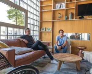 Twee mannen zitten in een moderne kantoorruimte aan de Overschiestraat 65 in Amsterdam met een houten wand, glazen bouwstenen en een loungehoek.